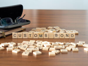 Scrabble tiles spelling out the words “CUSTOMS BOND” next to a pair of reading glasses on a table in El Paso.