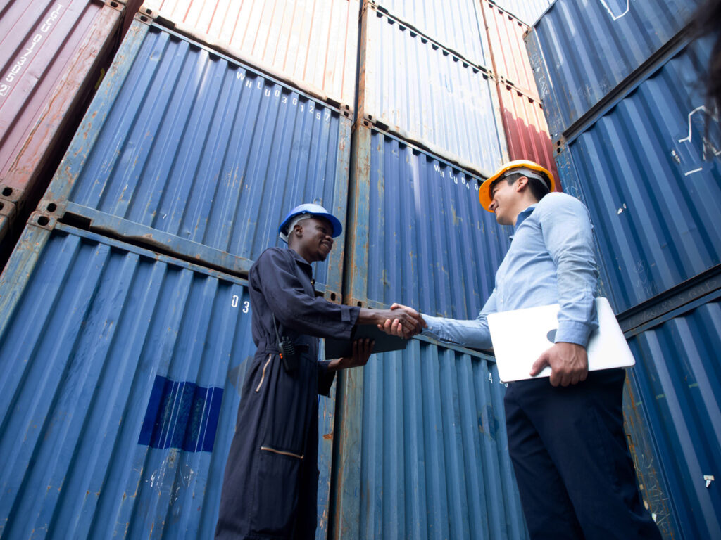 Two people shaking hands in front of blue cargo containers in El Paso.